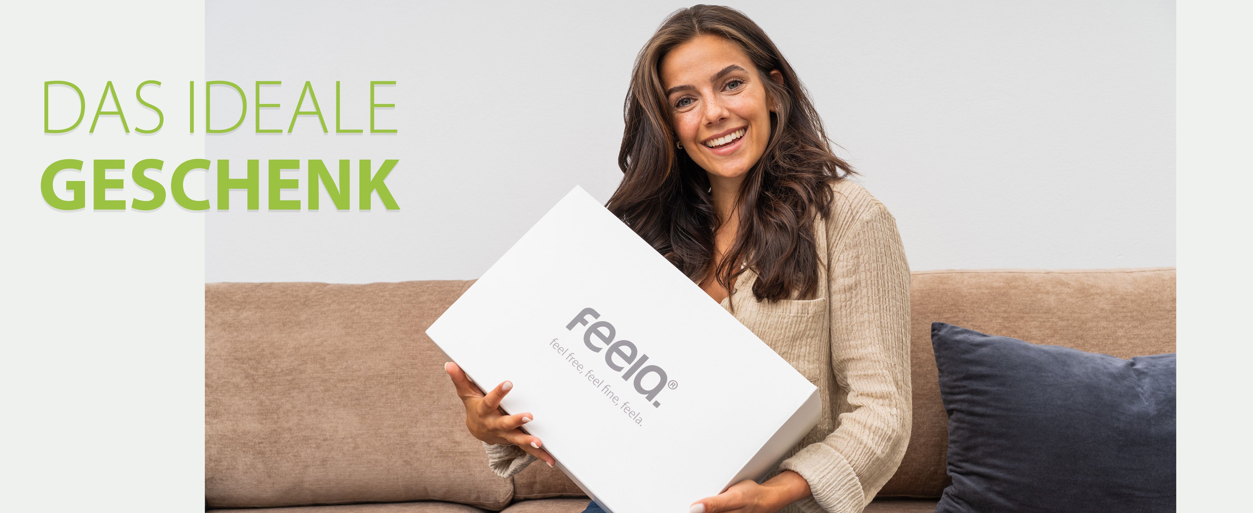 Das ideale Geschenk: Eine Frau hält lächelnd eine weiße Box mit dem feela-Logo, symbolisch für das Geschenk einer ergonomischen Fußstütze von feela.