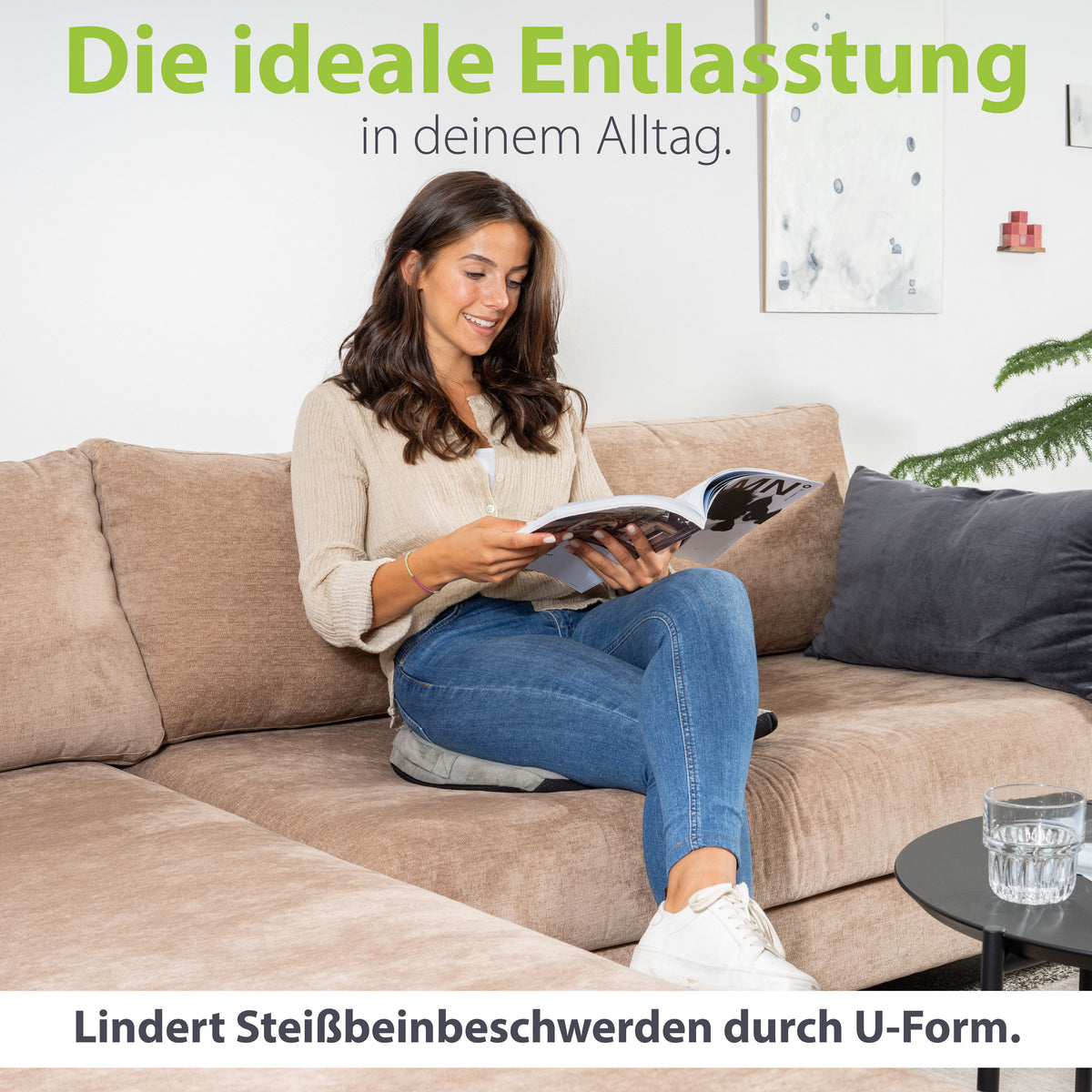 Entspannte Frau sitzt auf einem Sofa und liest ein Magazin, wobei sie ein U-förmiges Kissen benutzt, das als ideale tägliche Entlastung für Beinbeschwerden dargestellt wird.